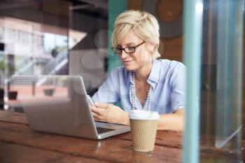 Businesswoman Using Phone Working On Laptop In Coffee Shop