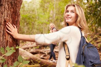 Girl touching a tree in a forest, her mother in the background
