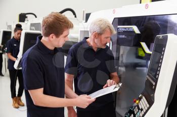 Male Apprentice Working With Engineer On CNC Machinery