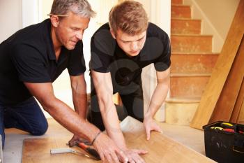 Two men laying wood panel flooring in a house