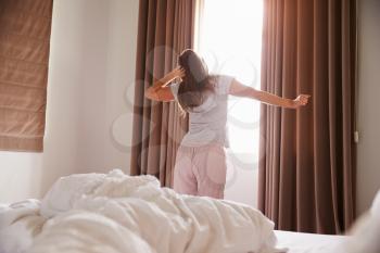 Woman Standing By Bedroom Window In Morning And Stretching