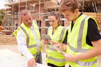 Builder On Building Site Discussing Work With Apprentices