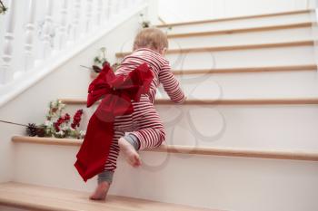 Toddler With Christmas Bow On Stairs In Pajamas