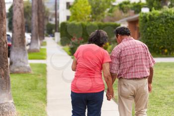 Senior Hispanic Couple Walking Along Sidewalk Together