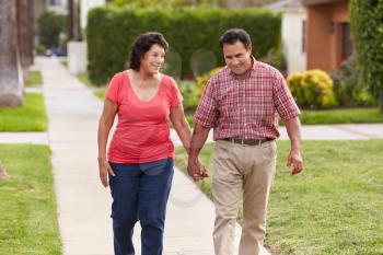 Senior Hispanic Couple Walking Along Sidewalk Together