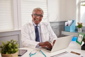 Senior black male doctor at an office desk looking to camera