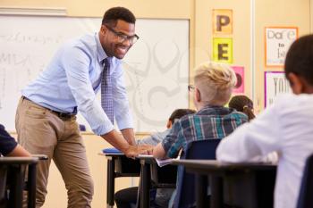 Smiling teacher leaning on elementary school pupils desk