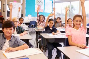 Elementary school kids in a classroom raising their hands