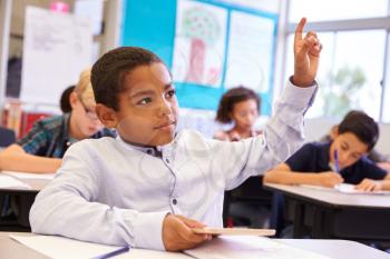 Boy with tablet raising his hand in elementary school class