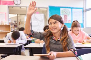 Girl with tablet raising hand in elementary school class