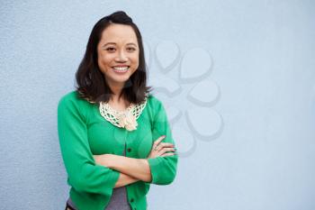 Waist up portrait of smiling Asian woman against grey wall