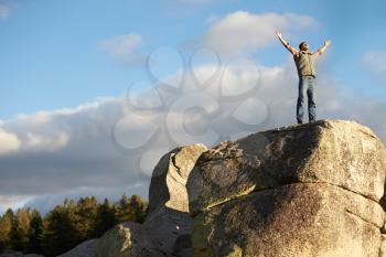 Man standing on rocky outcrop with arms raised