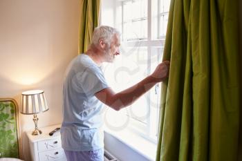 Middle aged man gets up and opens the curtains in hotel room