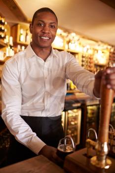 A young black man working behind a bar looks to camera