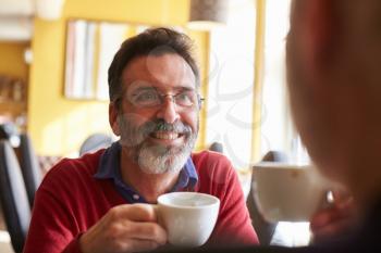 Male couple drink coffee at a restaurant, over shoulder view