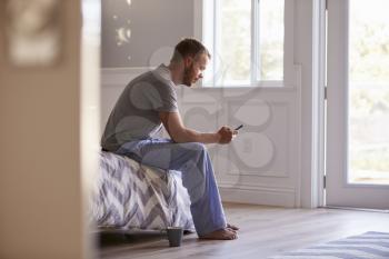 Man Wearing Pajamas Using Mobile Phone In Bedroom