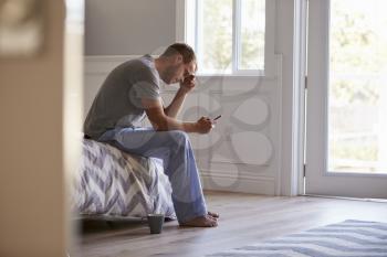 Stressed Man Wearing Pajamas Using Mobile Phone In Bedroom
