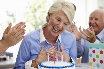 Senior Woman Blows Out Birthday Cake Candles At Family Party