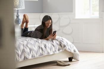 Woman Relaxing On Bed Checking Mobile Phone