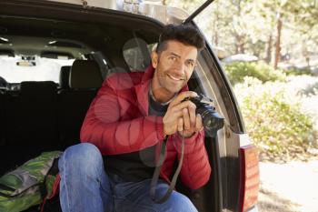 Portrait of man in the open back of car holding camera