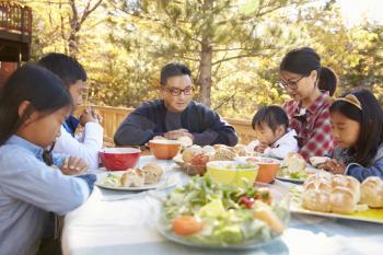 Asian family at a table on a deck say a prayer before eating