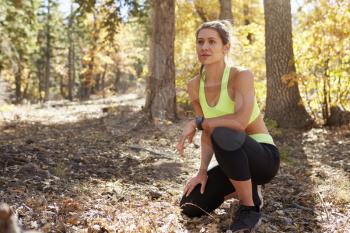Female runner kneeling in a forest, looking away