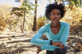 Young black woman in a forest checking smartwatch looks away