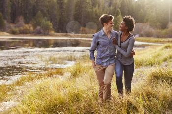 Mixed race couple embracing, walking near a rural lake
