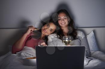 Female couple relax in bed with a laptop computer and drinks