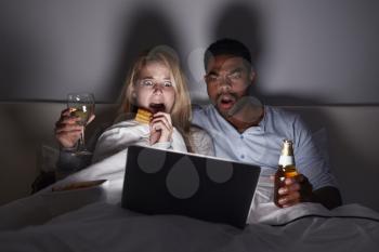Mixed race couple watching scary film in bed on laptop