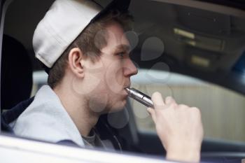 Young Man Sitting In Car Using Vapourizer