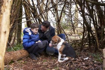 Father and son talking, under a shelter of branches with dog