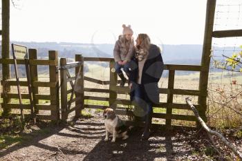 Mum and daughter by rural gate with dog look at each other