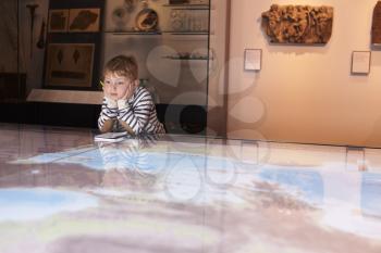 Boy On Trip To Museum Looking At Map And Writing In Notebook