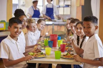 Kids at a table in a primary school cafeteria look to camera