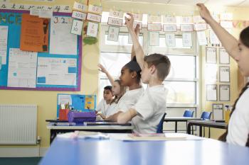 Primary school children raising hands in class, low angle