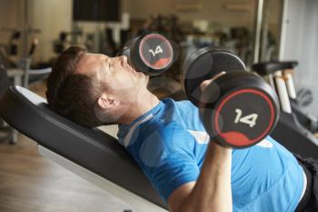 Man works out with dumbbells on a bench at a gym, side view