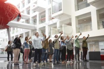 Students in a university atrium taking photos with phones
