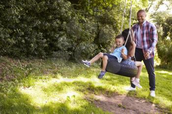 Father Pushing Children On Tire Swing In Garden