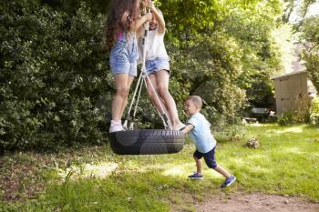 Group Of Children Playing On Tire Swing In Garden