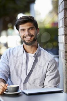 Bearded young man with laptop sitting outside cafe, vertical