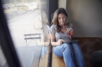 Young woman sits beside window in cafe using tablet computer