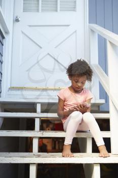 Young Girl Sits On Outdoor Steps Playing With Mobile Phone
