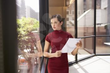 Businesswoman holding document, looking out of office window