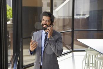 Smiling middle aged Hispanic businessman on phone in office