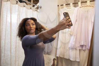 Woman taking selfie in a boutique changing room