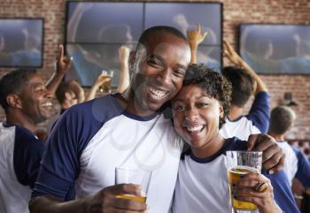 Portrait Of Couple Watching Game In Sports Bar On Screens