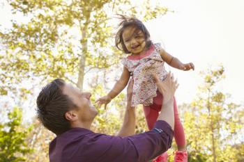 Father throwing his young daughter in the air in a park