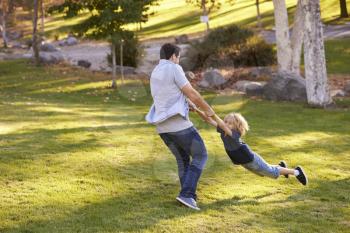 Father Swinging Son By His Arms In Park
