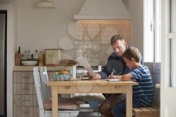 Father Helping Son With Homework Sitting At Kitchen Table